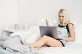 Happy casual beautiful woman working on a laptop sitting on the bed in the house. Royalty Free Stock Photo