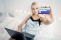 Woman sitting on bed with laptop holding credit card ordering shopping online in room background. Royalty Free Stock Photo