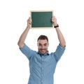 Happy casual man holding green blackboard above his head, smiling