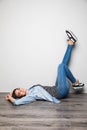 Happy casual woman lying on the floor with raised legs up over gray background and looking at camera Royalty Free Stock Photo