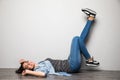 Happy casual woman lying on the floor with raised legs up over gray background and looking at camera Royalty Free Stock Photo