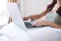 Happy casual woman sitting and using computer laptop on white pillow in bedroom. Young adult female Working from home or online Royalty Free Stock Photo