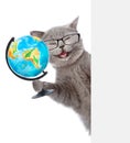 Happy cat in glasses holding globe and peeking from behind empty board. isolated on white background