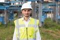 Happy caucasian adult engineer in helmet smiling at camera at high voltage power station outside. Positive worker