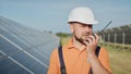 Happy caucasian adult engineer in helmet smiling at camera at solar power station outside. Ecological industry. Solar