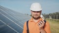 Happy caucasian adult engineer in helmet smiling at camera at solar power station outside. Ecological industry. Solar