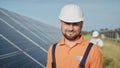 Happy caucasian adult engineer in helmet smiling at camera at solar power station outside. Ecological industry. Solar