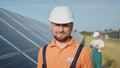 Happy caucasian adult engineer in helmet smiling at camera at solar power station outside. Ecological industry. Solar