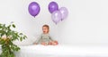 Happy caucasian baby girl,toddler of 1,2 year old sitting on bed holding balloons of very peri trendy color on white Royalty Free Stock Photo