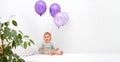 Happy caucasian baby girl,toddler of 1,2 year old sitting on bed holding balloons of very peri trendy color on white Royalty Free Stock Photo