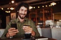 Happy caucasian bearded man holding mobile phone typing card data to make online payment sitting in cafe Royalty Free Stock Photo