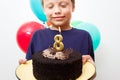 Happy caucasian boy celebrates birthday by holding a chocolate cake in his hands with candle and enjoying holiday Royalty Free Stock Photo