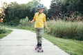 Happy Caucasian boy in grey helmet riding skateboard on road in park on summer day. Seasonal outdoor children activity sport. Royalty Free Stock Photo