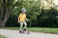 Happy Caucasian boy in grey helmet riding skateboard on road in park on summer day. Seasonal outdoors children activity sport. Royalty Free Stock Photo