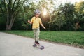 Happy Caucasian boy in grey helmet riding skateboard on road in park on summer day. Seasonal outdoors children activity sport. Royalty Free Stock Photo