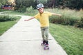 Happy Caucasian boy in grey helmet riding skateboard on road in park on summer day. Seasonal outdoors children activity sport. Royalty Free Stock Photo