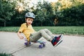 Happy Caucasian boy in grey helmet riding skateboard on road in park on summer day. Seasonal outdoors children activity sport. Royalty Free Stock Photo