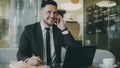 Happy Caucasian businessman sitting, smiling, talking on smartphone with partner and writing down information in notepad Royalty Free Stock Photo