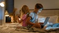 Happy caucasian children boy girl brother sister sibling friends playing online video game together on bed at home Royalty Free Stock Photo