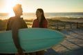 Happy caucasian couple on beach by the sea during susnset carrying surfboard smiling