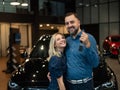 Happy caucasian couple hugging and man holding new car keys in car showroom. Royalty Free Stock Photo