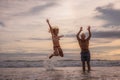 Happy Caucasian couple jumping on the beach. Motion body. Cheerful young man and woman enjoying life. Sunset time. Cloudy sky. Royalty Free Stock Photo