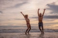 Happy Caucasian couple jumping on the beach. Motion body. Cheerful young man and woman enjoying life. Sunset time. Cloudy sky. Royalty Free Stock Photo