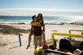 Happy caucasian couple next to beach buggy by the sea piggybacking