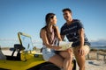 Happy caucasian couple sitting on beach buggy by the sea reading roadmap smiling Royalty Free Stock Photo