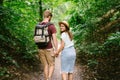 Happy caucasian couple are walking in a dense forest along the path holding hands, rear view. Hikers with backpack looking for Royalty Free Stock Photo