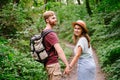 Happy caucasian couple are walking in a dense forest along the path holding hands, rear view. Hikers with backpack looking for Royalty Free Stock Photo