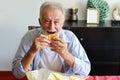 Happy caucasian elderly eating hamburger in living room with smiling face