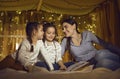 Mother and daughters reading fairytale in kids tent decorated with light garland Royalty Free Stock Photo