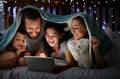 Happy caucasian family with two children using digital tablet lying under blanket in the dark at night with their faces Royalty Free Stock Photo