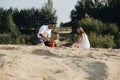 Happy caucasian family in white dress, mother and dad playing with little girl with sand toys playing in sandbox at