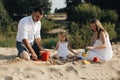 Happy caucasian family in white dress, mother and dad playing with little girl with sand toys playing in sandbox at Royalty Free Stock Photo