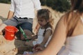 Happy caucasian family in white dress, mother and dad playing with little girl with sand toys playing in sandbox at