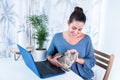 Happy Caucasian female on a desk petting her pet cat lying on the laptop at home Royalty Free Stock Photo