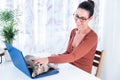 Happy Caucasian female with glasses on desk petting her pet cat lying on laptop at home Royalty Free Stock Photo