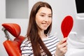 Happy caucasian female patient looking at mirror after dental treatment in clinic. Cheerful woman sitting in chair in dental Royalty Free Stock Photo