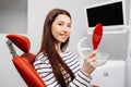 Happy caucasian female patient looking at mirror after dental treatment in clinic. Cheerful woman sitting in chair in dental Royalty Free Stock Photo