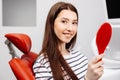 Happy caucasian female patient looking at mirror after dental treatment in clinic. Cheerful woman sitting in chair in dental Royalty Free Stock Photo