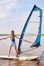 smiling woman stands on windsurf and holds the sail. Windsurfing on lake water