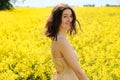 Happy caucasian girl with curly hair in canola field with yellow flowers on sunny summer day, closeup portrait. Young woman Royalty Free Stock Photo