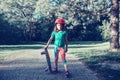 Happy Caucasian girl in pink helmet riding skateboard on road in park on summer day. Seasonal outdoors children activity sport. Royalty Free Stock Photo