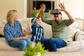 Happy caucasian grandmother and grandson watching grandfather wearing vr headset on couch at home