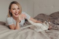 Happy Caucasian laughing smiling blonde woman lying on bed in bedroom at home and playing with oriental point-colored cat Royalty Free Stock Photo