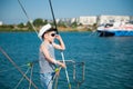 Happy caucasian little boy in white captain hat and striped tank top with denim shorts standing on luxury yacht board adjusting