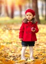 Happy caucasian little girl in a red coat and beret in the park with a red apple Royalty Free Stock Photo