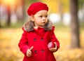 Happy caucasian little girl in a red coat and beret in the park with red apple in her hands Royalty Free Stock Photo